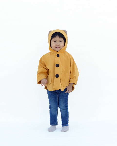 Toddler girl in golden yellow kitten cape coat jacket with cat ears and face on the hood, cat paw pockets, and buttons in the front 