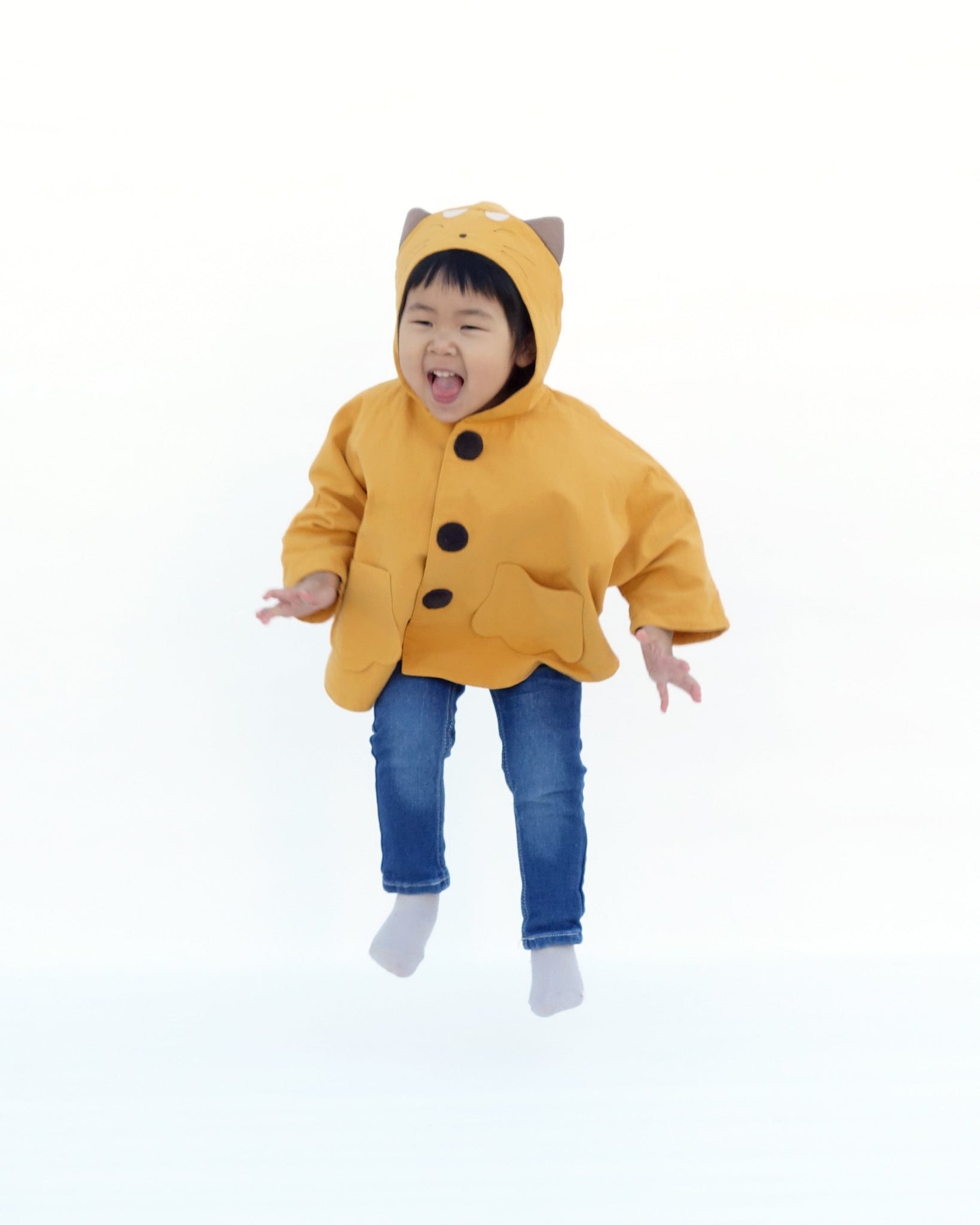Toddler girl in golden yellow kitten cape coat jacket with cat ears and face on the hood, cat paw pockets, and buttons in the front 