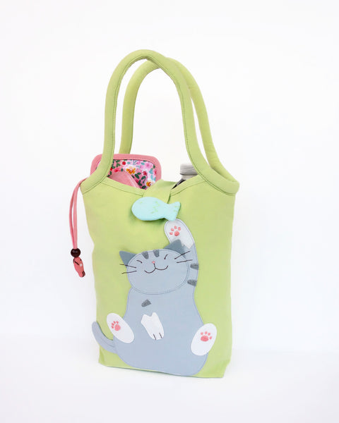 Cat Bottle-Tote in green with cotton interior, nylon lining, cat appliqué, embroidery detail, large main compartment, Velcro flap closure, sturdy double padded handles, squared off bottom for holding books, wallet, water bottle, pencil pouch, or umbrella.