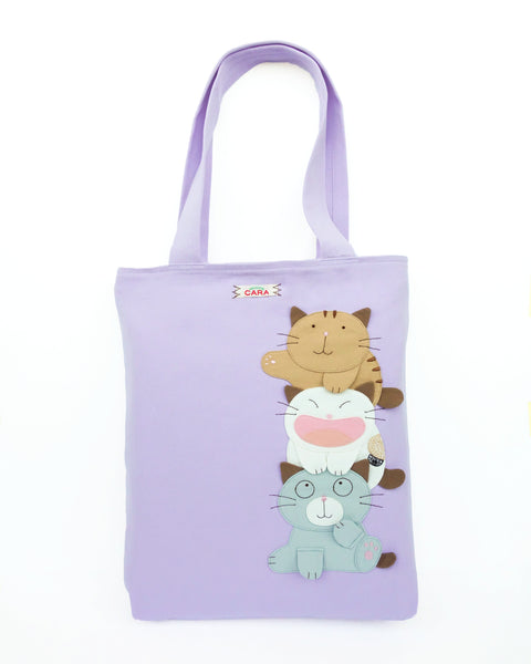 A lilac purple cat-themed canvas tote bag with three appliqué cats playfully stacked on top of each other